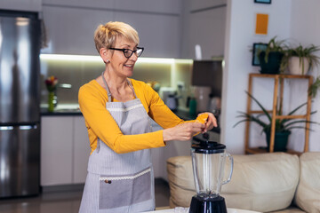 Senior woman in casual home clothes prepares healthy cocktails with different seasonal fruits.