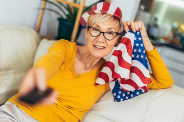 Obraz premium Elderly woman holding an American flag at home.