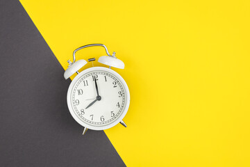 White alarm clock on a yellow and green background, flat lay.