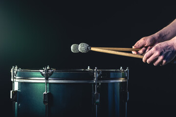 A man plays a musical percussion instrument with sticks on a dark background.