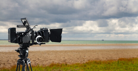 Digital movie camera making film in nature. 
a video camera films on a beach. Wide background with copy space for documentary production. - obrazy, fototapety, plakaty