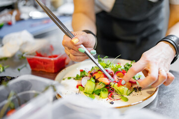 Chef cooking Green salad with salmon, cucumbers, lettuce, spices, caviar on restaurant kitchen