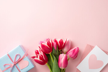 Mother's Day atmosphere concept. Top view photo of bouquet of fresh tulips blue giftbox pink envelope and postcard with heart on isolated pastel pink background with empty space