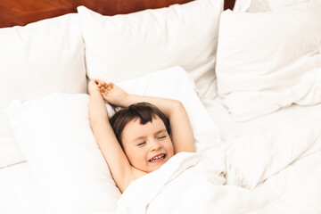 Fototapeta na wymiar Little boy lying and stretching his arms in the bed at home in the morning. Home lifestyle boy relaxing sleeping on bed in bedroom.
