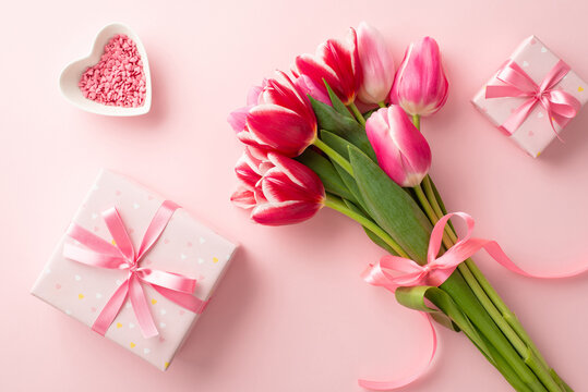 Mother's Day concept. Top view photo of bouquet of pink tulips tied with ribbon gift boxes with bows and heart shaped saucer with sprinkles on isolated pastel pink background