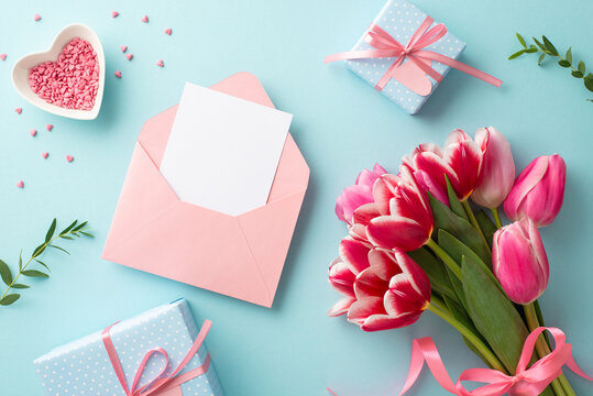 Mother's Day concept. Top view photo of bunch of tulips gift boxes with bows envelope with paper sheet and heart shaped saucer with sprinkles on isolated pastel blue background with blank space