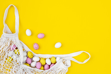 Colored Easter eggs in a mesh bag on a yellow background, flat lay.