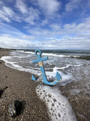 blauer Anker steht am Strand in der Brandung der Ostsee 