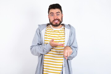Young caucasian mán wearing trendy clothes over white background In hurry pointing to watch time,...