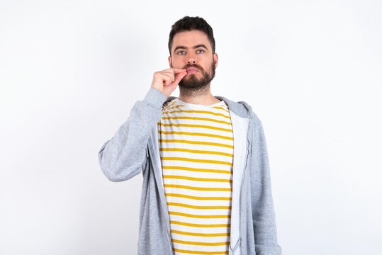 Young caucasian m&aacute;n wearing trendy clothes over white background mouth and lips shut as zip with fingers. Secret and silent, taboo talking.