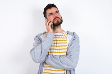 Sad Young caucasian m&aacute;n wearing trendy clothes over white background talking on smartphone. Communication concept.