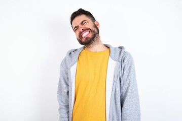 Positive Young caucasian mán wearing trendy clothes over white background with overjoyed expression closes eyes and laughs shows white perfect teeth