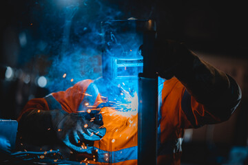 Closeup workers wearing industrial uniforms and using electric arc welding machine to weld steel at...