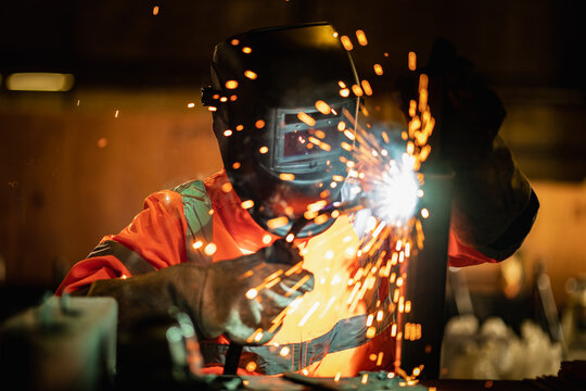 Closeup workers wearing industrial uniforms and using electric arc welding machine to weld steel at factory. Metalwork manufacturing and construction maintenance service by manual skill labor concept.