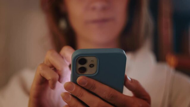 Close-up face of young serious Caucasian businesswoman using mobile app working online with smartphone in blue case.