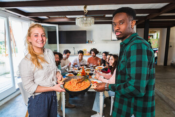 Mixed couple showing off a pot of spaghetti at a friends lunch