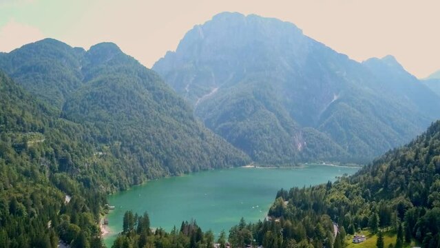 Aerial 4K footage of Lagodel Predil in Italy showcases the stunning alpine lake, nestled among the snow-capped peaks of the Julian Alps, surrounded by the natural beauty of the region.