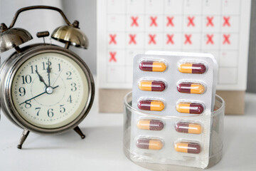 long term schedule medication with antibiotics pills , calendar and alarm clock on desk