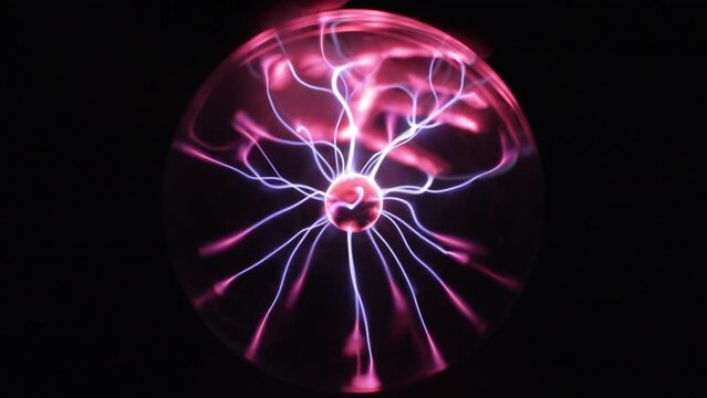 Hand holding a plasma globe in slow motion. Blue and purple light beams and energy rays inside the ball. Full sphere on black background. Tesla coil electric discharge.