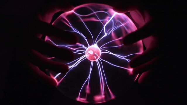Hands touching a plasma globe in slow motion. Blue and purple light beams and energy rays inside the ball. Full sphere on black background. Tesla coil electric discharge.