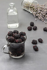 Fototapeta na wymiar Blackberries in a glass mug with water. Water bottle. Lavender on the table.