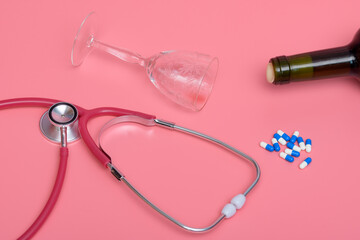 Przewrócona butelka i kieliszek od wina obok stetoskopu na różowym tle - obrazy, fototapety, plakaty