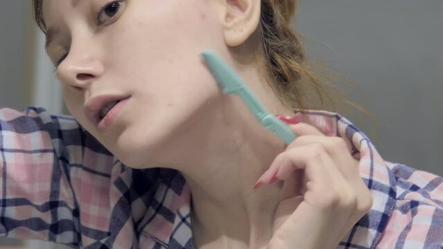 The 4k footage of a woman using a facial razor to shave the hair on her face during her skincare routine