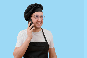 Young smiling chef talking on the phone on a blue background.