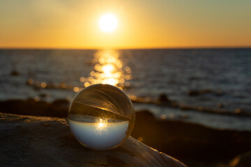Ball made of glass lies on a stone in which the beach and the sea are reflected