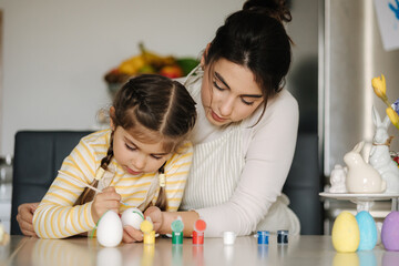 Portrait of mom and daughter painting easter eggs on kitchen. Spring holidays mood. Family