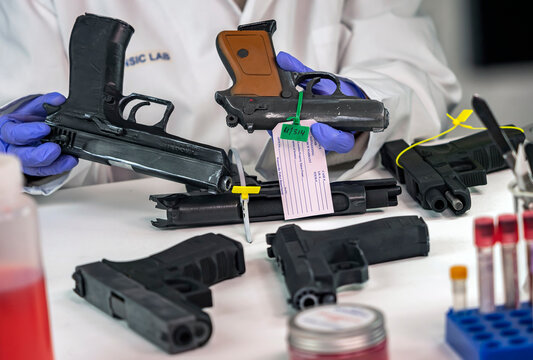 Police scientist analyzes several automatic pistols in crime lab, conceptual image