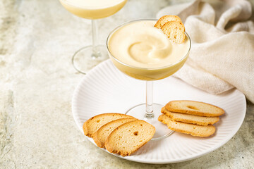Zabaione or sabayon, or advocaat in a champagne coupe, alcoholic creamy drink  or dessert. Cream made with egg yolks, sugar, and a sweet wine Marsala or liqueur. Baicoli biscuits.  - obrazy, fototapety, plakaty