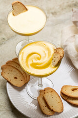 Zabaione or zabaglione or sabayon in a champagne coupe.  Italian cream-based dessert, made with egg yolks, sugar,  sweet wine Marsala or liqueur. Light custard, whipped cream. Baicoli biscuit.