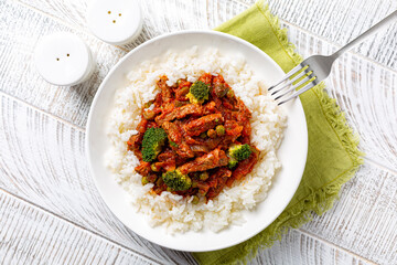 Homemade beef stew and vegetables, green peas, broccoli, tomato sauce  with rice. Top view, white wooden background.