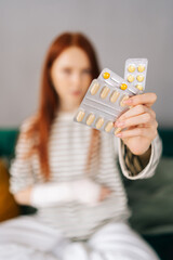 Vertical selective focus shot portrait of unrecognizable young woman with broken right hand wrapped in gypsum bandage holding blister packs of pills at home. Concept of insurance and healthcare