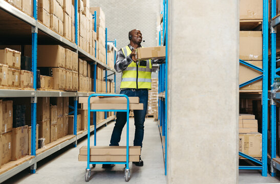 Happy warehouse worker pulling a flat while picking orders