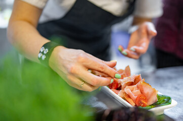 Chef decorate ready dish with slices parma ham on restaurant kitchen