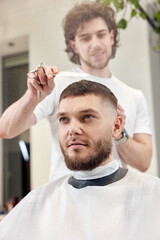 hairdresser does haircut for man using comb and grooming scissors