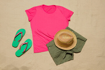 Sand beach texture background. Mockup pink summer t-shirt outfit copy space. Blank template woman shirt Top view. Summertime accessories hat, flip-flops, jeans. Flat-lay closeup tshirt on seashore.