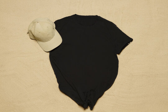 Sand Beach Texture Background. Mockup Black Summer T-shirt Copy Space. Blank Template Shirt Top View. Summertime Clothing Baseball Hat. Flat-lay Closeup Tshirt On Seashore. Beachtime Holidays