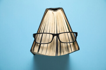 Eyeglasses and book on the blue background.
