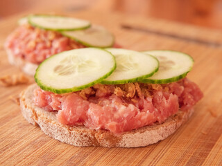 Savor a rustic German snack with Onion Mett, topped with crunchy Rostzwiebel (crispy fried onions), and refreshing slices of Gurken (cucumbers), all served on freshly baked bread.