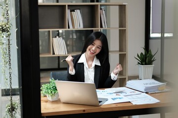 Fototapeta na wymiar Asian businesswoman raising hands happily with successful plan with happy smile with laptop computer.