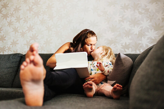 Mother with daughter (2-3) on sofa using tablet