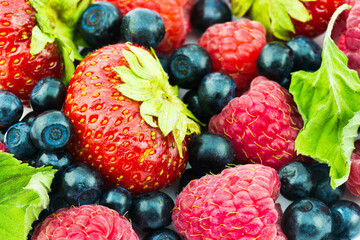 Close-up view of fresh strawberries, blueberries and raspberries with green green leaves