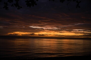Picturesque sunset on the beach of Siquijor in the Philippines, the cloudy sky shines in golden yellow orange and red colors, in the foreground treetops.