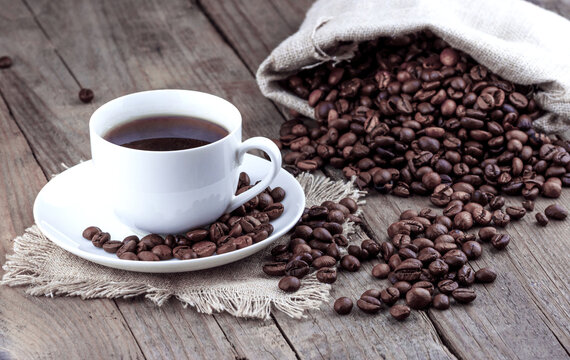 White cup of coffee with roasted coffee beans on old wooden background
