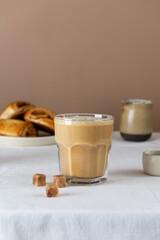 Fresh coffee cappuccino in a glass with cinnamon buns and cane sugar on table, rustic style.