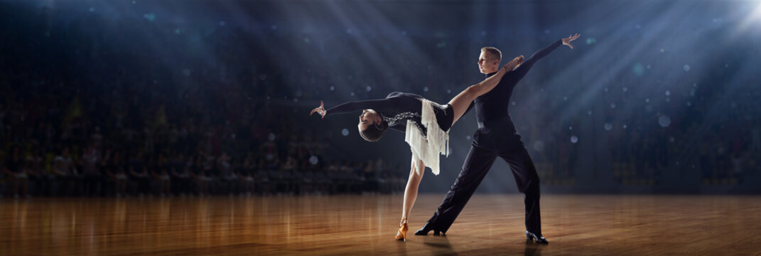 Dance aesthetics. Talented young man and girl in beautiful costumes performing, dancing tango and ballroom dance under spotlights. 3D audience background. Concept of art, movements, beauty, hobby