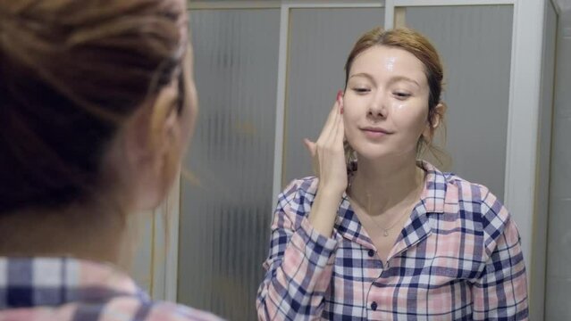 The 4k video of a woman using a natural stone massage tool to massage her under-eye area while applying an eye mask during her skincare routine.